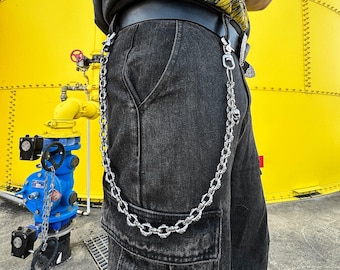 May include: A person wearing black jeans with a silver chain attached to their belt loop. The chain has a skull charm at the end. The person is standing in front of a yellow wall.