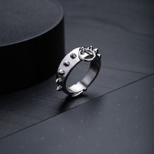 May include: A silver ring with a circle design and spikes around the band.