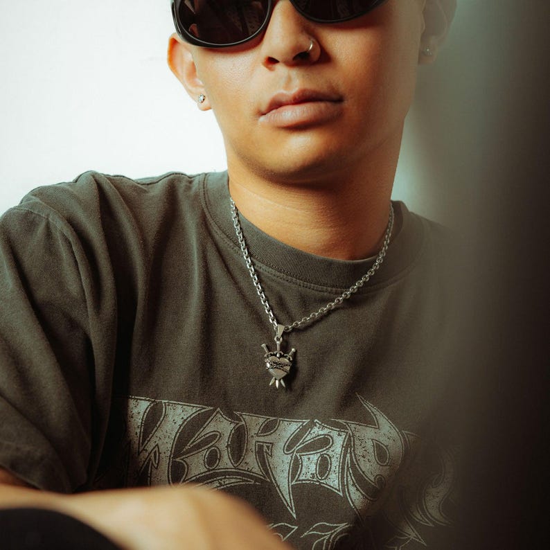 Silver heart pendant with 3 swords going through it and wrapped in chain on male model with sunglasses
