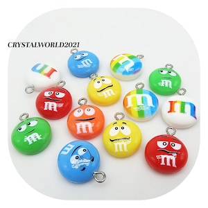 Puede incluir: Surtido de 12 abalorios redondos de colores con el logotipo de M&M's y diversas expresiones faciales. Cada abalorio tiene un lazo plateado para sujetarlo a joyas u otras manualidades.