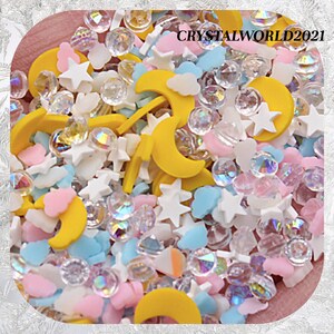Pode incluir: Uma mistura de granulados coloridos com luas crescentes amarelas, estrelas brancas, nuvens azuis e rosadas e contas transparentes iridescentes. Os granulados são perfeitos para decorar bolos, cupcakes, biscoitos e outras guloseimas. CRYSTALWORLD2021 está impresso na imagem.