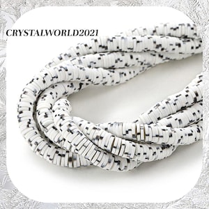 May include: White ceramic beads with black speckles. The beads are round and have a slightly irregular shape. They are strung together in a long strand.