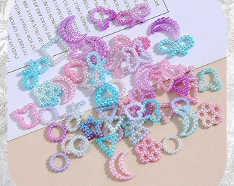 Könnte beinhalten: Eine Sammlung pastellfarbener, perlenbesetzter Verzierungen in verschiedenen Formen, darunter Herzen, Sterne, Monde und Blumen. Die Perlen sind in Rosa-, Blau- und Lilatönen gehalten. Der Text "CRYSTALWORLD2021" befindet sich unten.