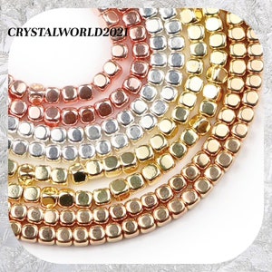 May include: A close-up of a strand of square-shaped beads in various metallic colours, including gold, silver, and rose gold. The beads are arranged in a circular pattern, creating a decorative and eye-catching display.