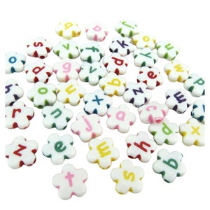May include: A scattering of white, flower-shaped beads, each displaying a different letter of the alphabet in various colours. The letters are in red, green, yellow, blue, and pink.