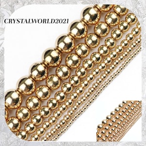 May include: Assortment of gold-toned round beads in various sizes. The beads are arranged in rows, with the largest beads at the top and the smallest beads at the bottom.  The beads are smooth and shiny.