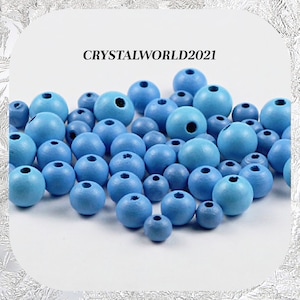May include: A large group of light blue wooden beads. The beads are round and have a hole in the centre. The beads are arranged in a random pattern.  CRYSTALWORLD2021
