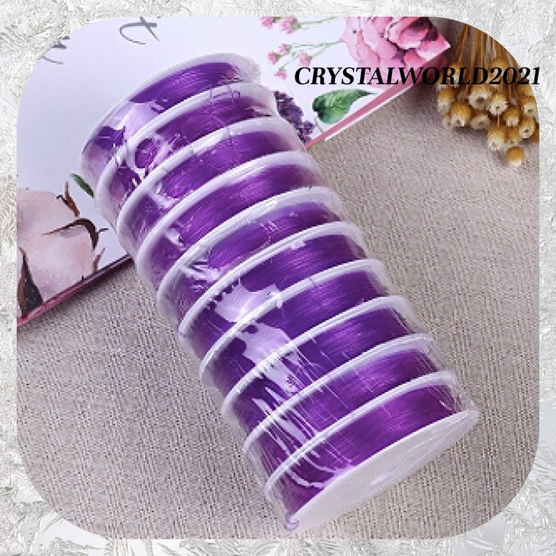 May include: A roll of purple elastic string for jewelry making, wrapped in clear plastic and packaged in a white cardboard tube.  The text "CRYSTALWORLD2021" is visible on the packaging.
