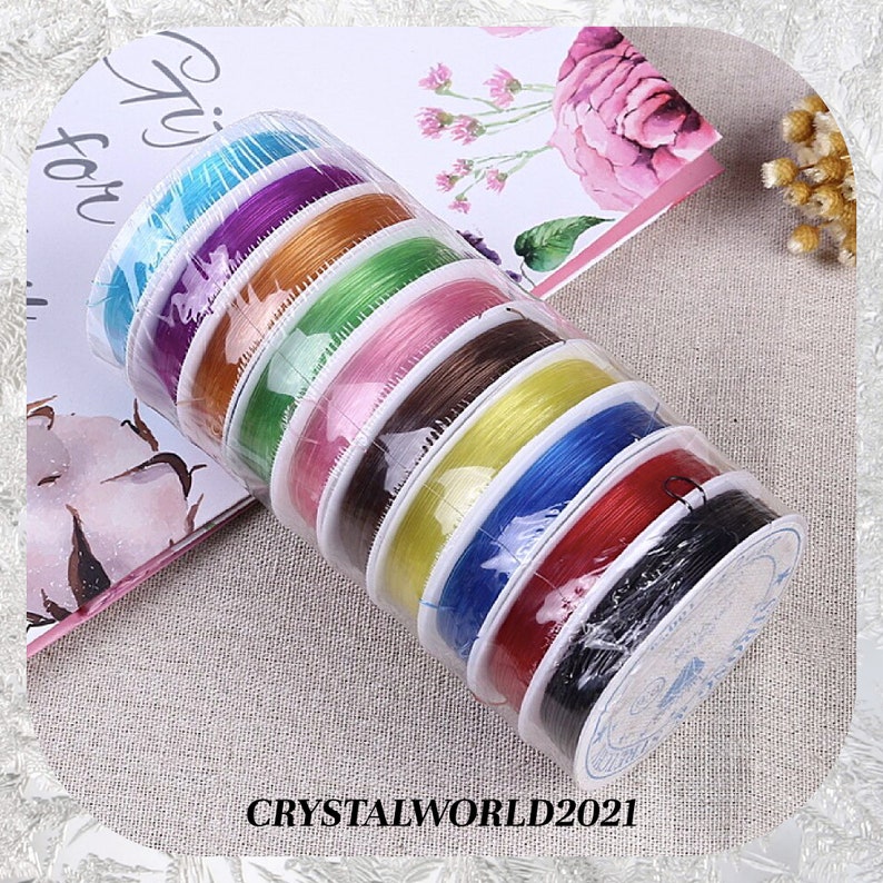 May include: A set of eight spools of elastic string in various colors, including blue, purple, orange, green, pink, brown, yellow, red, and black. The spools are wrapped in clear plastic and labeled with the text "CRYSTALWORLD2021".