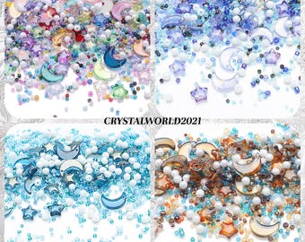 Può includere: Assortimento di perline di vetro colorate, stelle e mezze lune. Le perline sono in tonalità di blu, rosa, marrone e bianco. Le stelle e le lune sono in vetro trasparente.