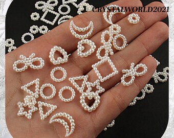 May include: A collection of small, white pearl-like beads in various shapes, including circles, squares, triangles, hearts, bows, and stars. The beads are scattered across a hand, with the text "CRYSTALWORLD2021" visible in the background.