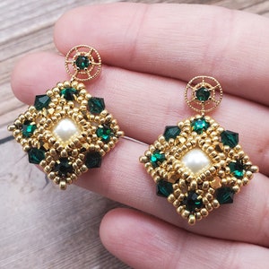 May include: Gold earrings with a square design featuring green and white beads. The earrings have a pearl-like bead in the center of the square.