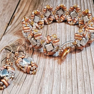 Puede incluir: Un conjunto de joyas de cuentas de cobre y plata que incluye un brazalete y pendientes. El brazalete es de diseño espiral con una combinación de colores cobre y plata. Los pendientes tienen forma de lágrima y presentan una combinación de colores cobre y plata.