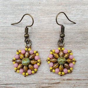 May include: A pair of dangle earrings featuring a hexagonal flower design. The flower is crafted from brown, pink, and yellow beads with a green centre.