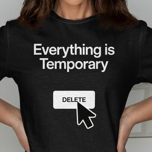 May include: Black t-shirt with the text "Everything is Temporary" in white. Below the text is a white rectangle with the word "DELETE" and a cursor icon. The shirt is short-sleeved.
