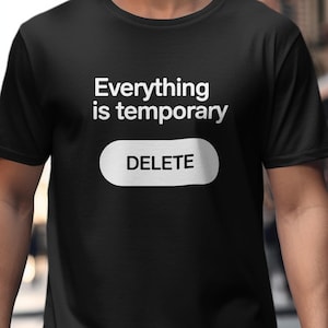 May include: Black t-shirt featuring the phrase "Everything is temporary" and a white button with "DELETE" printed on it. The shirt has a crew neck.