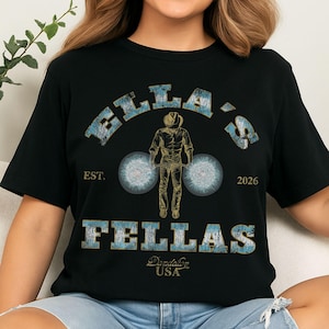 May include: Black t-shirt with the text "ELLA'S" above "FELLAS" and an astronaut graphic. The shirt also includes the text "EST. 2026" and "Made in the USA".