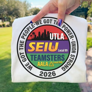 Op de afbeelding: Wit t-shirt met een cirkelvormige afbeelding. De afbeelding bevat de tekst "WE GOT THE PEOPLE - WE GOT THE POWER - UNION STRONG." Het bevat ook "UTLA," "SEIU," "TEAMSTERS," en "AALA," samen met het jaar "2026."