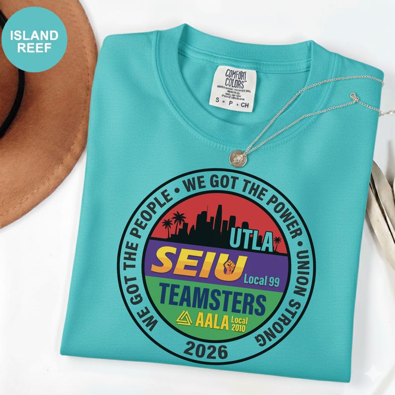 K&ouml;nnte beinhalten: Ein t&uuml;rkisfarbenes Comfort Colors T-Shirt mit Rundhalsausschnitt und Grafikdruck. Der Druck zeigt ein kreisf&ouml;rmiges Design mit dem Text "WE GOT THE PEOPLE" und "WE GOT THE POWER". Das Shirt hat auch den Text "SEIU TEAMSTERS AALA 2026".