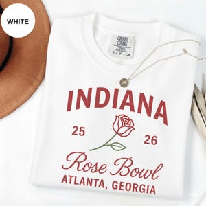 以下が含まれることがあります： 白のスウェットシャツ。マルーン色の「INDIANA」の文字、バラのグラフィック、「Rose Bowl ATLANTA, GEORGIA」の文字がプリントされています。スウェットシャツには数字の「25」と「26」もプリントされています。