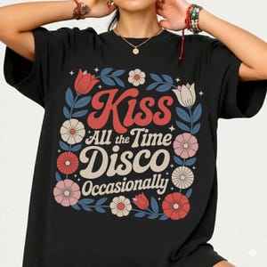 May include: Black t-shirt with a floral design and the words "Kiss All the Time Disco Occasionally" in red, cream, and white. The design includes flowers and leaves in red, pink, and blue.