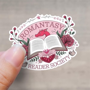 May include: A pink and white sticker featuring a dragon, an open book, and flowers. The text reads "Romantasy Reader Society".