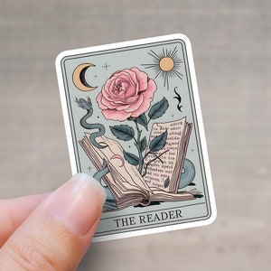 May include: A tarot card with a light blue background featuring a pink rose, a snake, and an open book. The card is titled "The Reader".