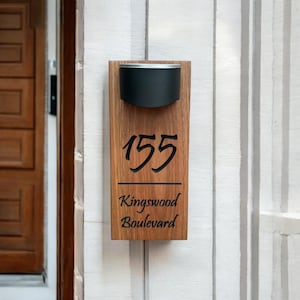 Puede incluir: Un letrero de número de casa de madera con una lámpara negra. El letrero dice "155 Kingswood Boulevard".