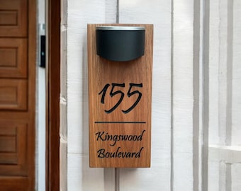 Könnte beinhalten: Ein rechteckiges Hausnummernschild aus Holz mit dunkelbrauner Holzmaserung. Das Schild zeigt die Zahl 155 und den Text Kingswood Boulevard in schwarzer Schrift. Ein schwarzes, halbkreisförmiges Lichtelement ist oben angebracht.