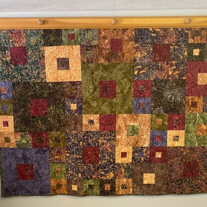 Könnte beinhalten: Ein Patchwork-Decken mit einer Vielzahl von braunen, grünen und violetten Quadraten. Die Decke ist aus verschiedenen Stoffen mit verschiedenen Mustern gefertigt.