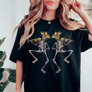 May include: Black oversized t-shirt with a graphic of two skeletons playing the violin while wearing sombreros.