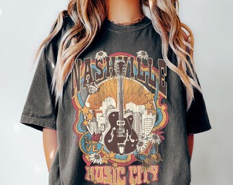May include: A black t-shirt with a vintage-style graphic of a guitar, cityscape, and the text "Nashville Music City".