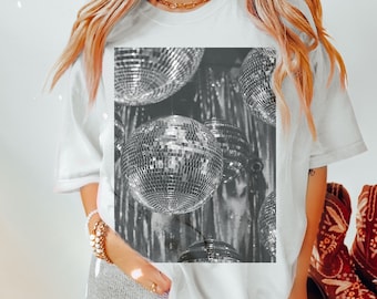 May include: A white t-shirt with a black and white graphic of disco balls. The graphic is centered on the shirt and features multiple disco balls of varying sizes.