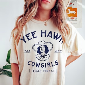 K&ouml;nnte beinhalten: Ein wei&szlig;es T-Shirt mit einer blauen Grafik einer Frau mit Cowboyhut und dem Text "Yee Haw!" "TRD" "MARK" "COWGIRLS" "TEXAS FINEST"