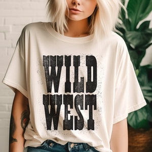 Puede incluir: Una camiseta blanca con un estampado gr&aacute;fico negro que dice "WILD WEST" en una fuente desgastada.