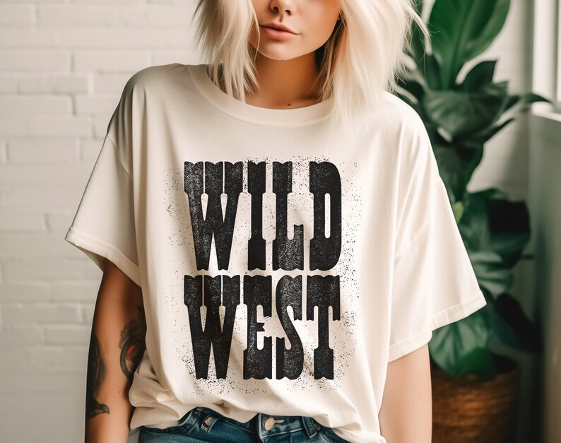 Puede incluir: Una camiseta blanca con un estampado gr&aacute;fico negro que dice "WILD WEST" en una fuente desgastada.