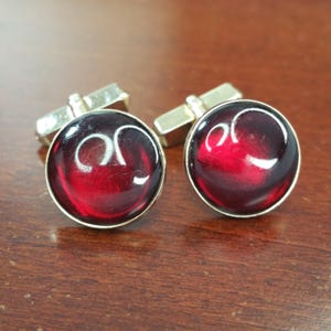 May include: A pair of cufflinks with red glass cabochons set in silver tone metal. The cabochons have a white swirl design.