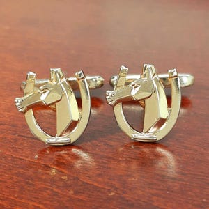 May include: A pair of gold-toned metal cufflinks, each featuring a stylized horse head silhouette centered within a horseshoe frame. The design includes a polished, reflective surface and a standard T-bar swivel mechanism on the back of each piece.