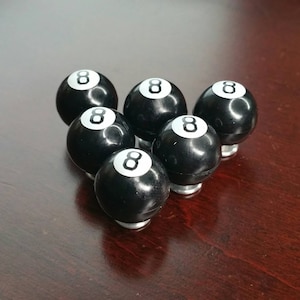 May include: Six black and white 8-ball billiard balls with a white number 8 on each ball.
