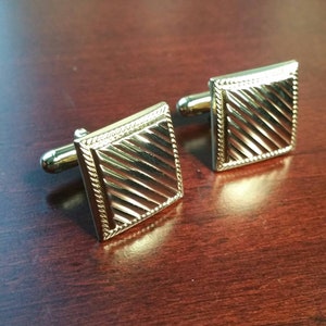 Peut inclure: Une paire de boutons de manchette dorés avec un motif carré et un motif diagonal. Les boutons de manchette ont une finition polie.