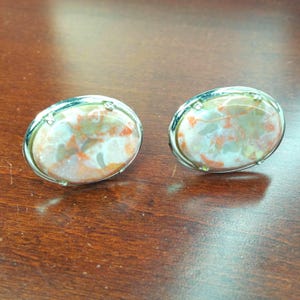 Puede incluir: Un par de pendientes ovalados de plata con una incrustación de piedra marmoleada blanca, naranja y marrón.