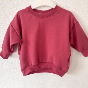 Könnte beinhalten: Ein roter Pullover mit langen Ärmeln und einem Rundhalsausschnitt.