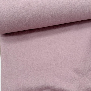 Könnte beinhalten: Eine Rolle weichen, malvenfarbenen Stoffes. Das Material hat ein strukturiertes, filzartiges Aussehen. Der Stoff ist eng gerollt und zeigt die Schichten des Materials. Die Farbe ist ein gedämpftes, staubiges Rosa.