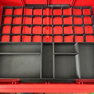 Może przedstawiać: Czerwone plastikowe pudełko na narzędzia z czarną kratką i kilkoma szarymi tacami do przechowywania. Wnętrze podzielone jest na przegródki do organizacji narzędzi i drobnych części. Pudełko jest otwarte.
