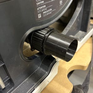 Puede incluir: Primer plano de una herramienta eléctrica negra con una boquilla negra y una base gris. La herramienta tiene la palabra "CAUTION" impresa, junto con otro texto. La herramienta está sobre una superficie de madera.