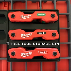 Peut inclure: Trois outils rouges Milwaukee dans un plateau noir, étiquetés avec "TORX", "MM" et "SAE". Les outils sont dans un bac de rangement gris et rouge. Le texte "THREE TOOL STORAGE BIN" est visible.