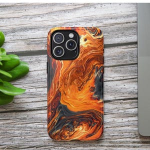 Puede incluir: Una funda de tel&eacute;fono con un dise&ntilde;o abstracto vibrante en tonos naranja, marr&oacute;n y negro. La funda tiene un acabado brillante y un recorte para la c&aacute;mara. La funda del tel&eacute;fono est&aacute; sobre una superficie de madera con hojas verdes y un port&aacute;til.