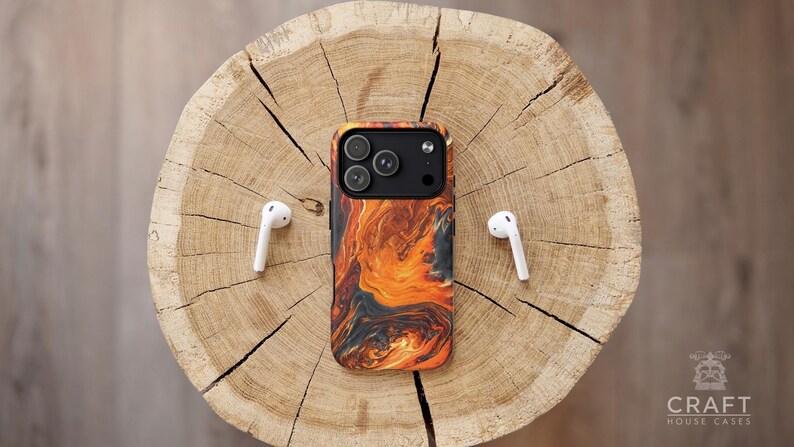 Puede incluir: Una funda de tel&eacute;fono con un dise&ntilde;o naranja y negro llameante, y auriculares inal&aacute;mbricos blancos se muestran sobre una superficie de madera. La funda del tel&eacute;fono tiene un m&oacute;dulo de c&aacute;mara con tres lentes. El logotipo de Craft House Cases es visible.
