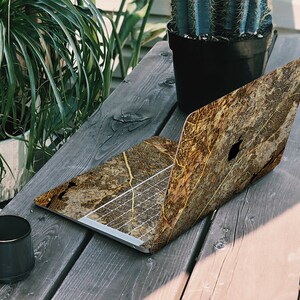 May include: A laptop computer with a brown and gold leaf pattern skin. The laptop is sitting on a wooden table with a cactus plant and a black mug in the background.