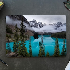 May include: A laptop skin with a scenic image of a mountain lake with snow-capped peaks and a blue sky. The lake is surrounded by trees and the water is a vibrant blue.